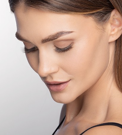 Seorang model melihat ke bawah dan tersenyum. Penekanan pada kening dan sebatannya.